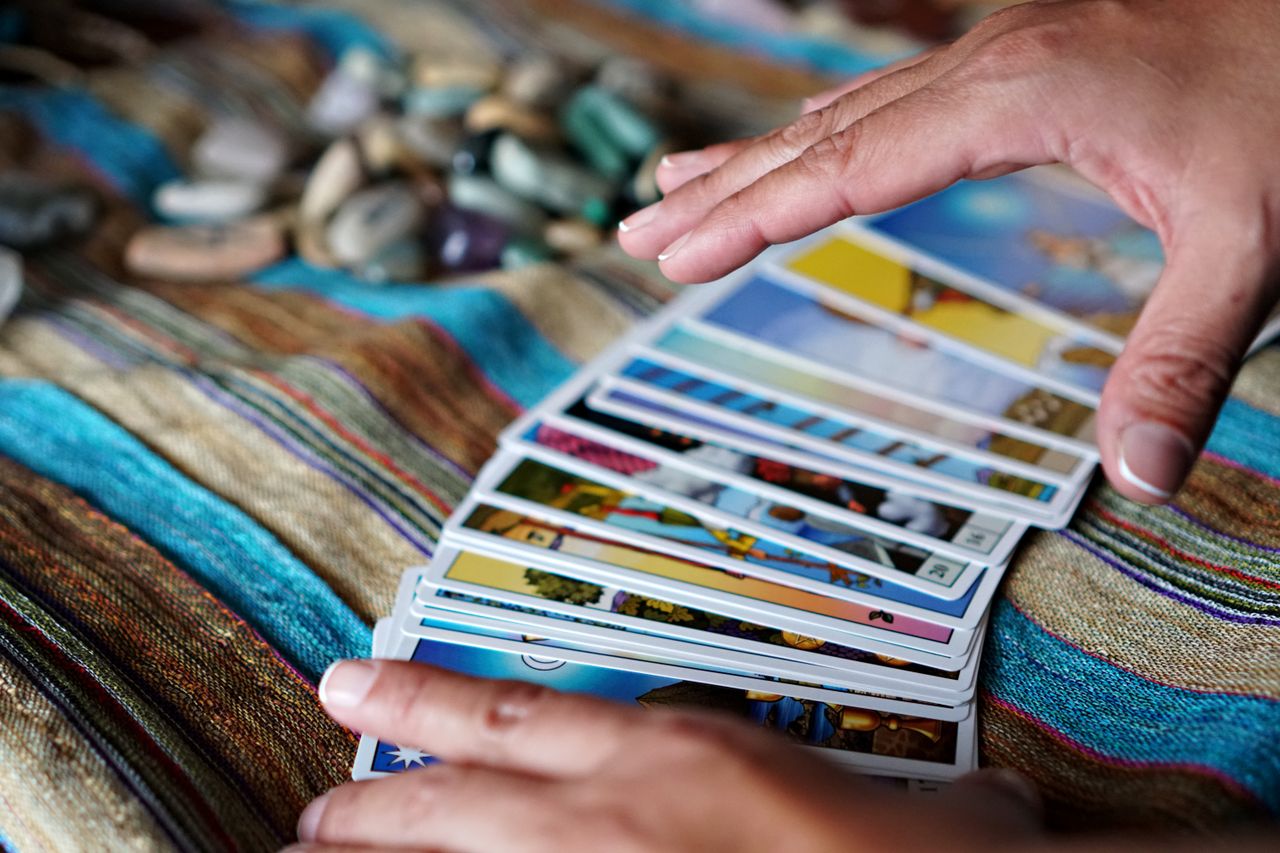 Hands arranging tarot cards on a vibrant woven cloth with stones nearby.