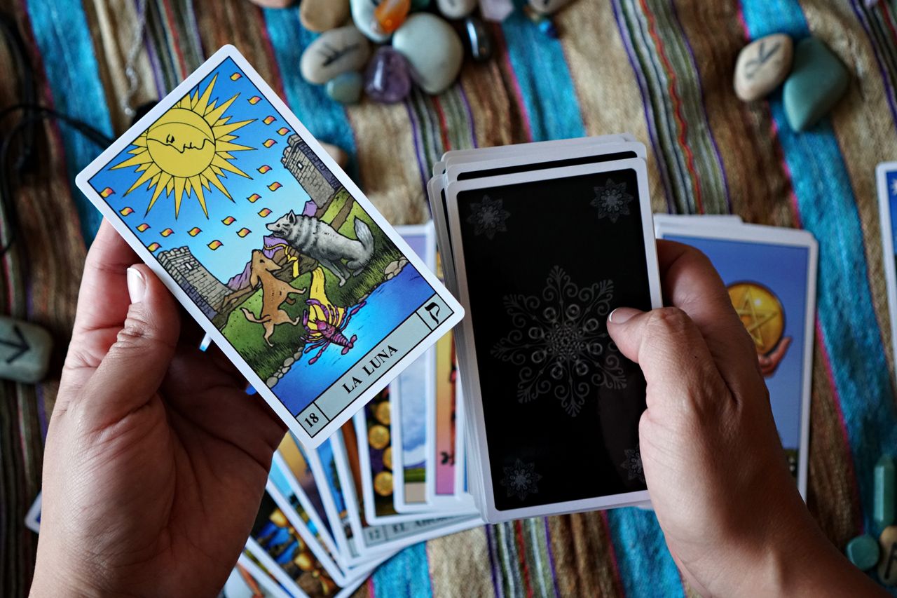 Close-up of hands holding tarot cards featuring 'La Luna' for a mystical reading.
