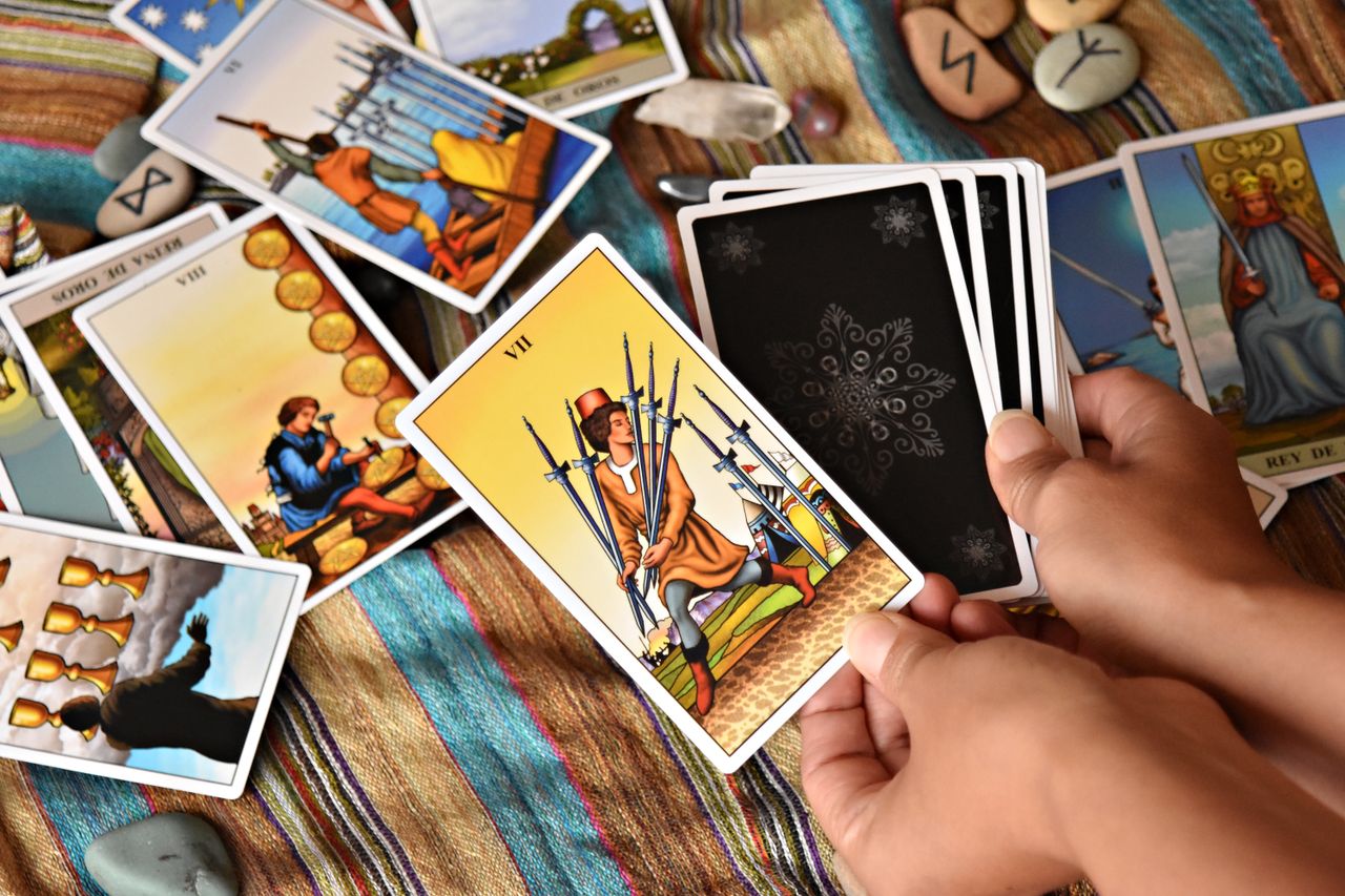 Hands holding tarot cards during a reading session on a colorful cloth background.