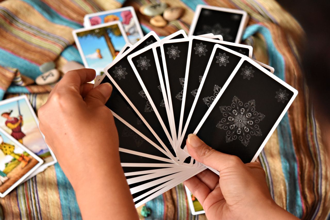 Close-up of hands holding tarot cards during a reading on a colorful cloth.